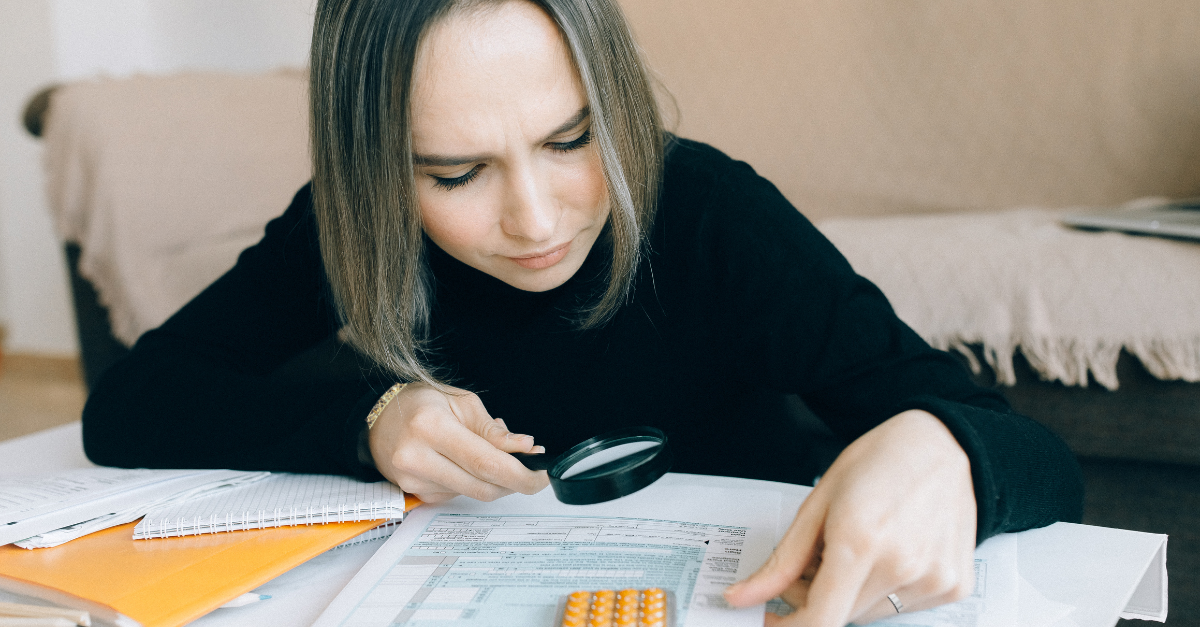 Woman using a magnifying glass to review paper tax forms