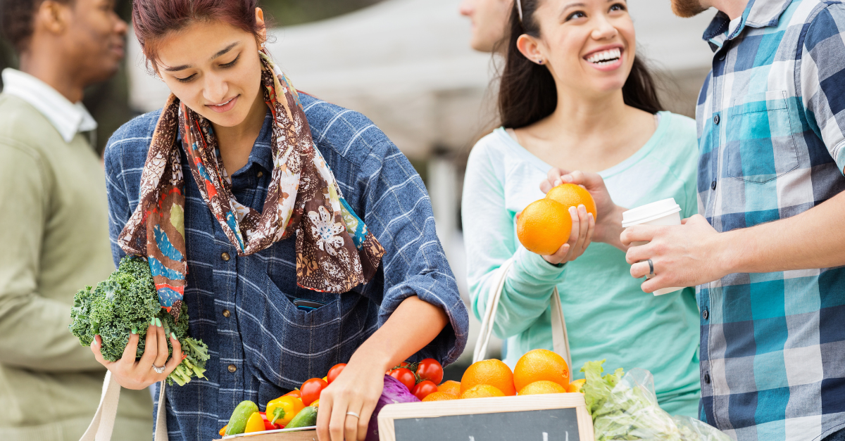 People at an open air market, looking at fruits and vegetables.