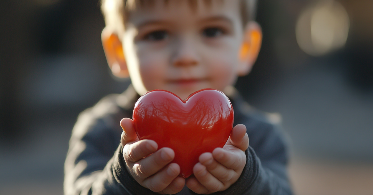 A little boy holding out a red, plastic heart