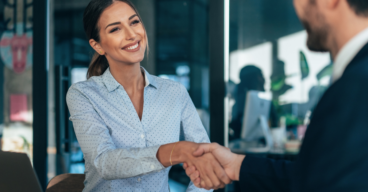 A smiling woman shaking a man's hand.