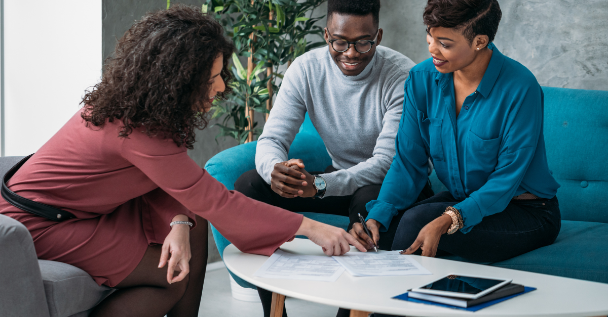 A couple sitting on a couch looking at documents with a third person