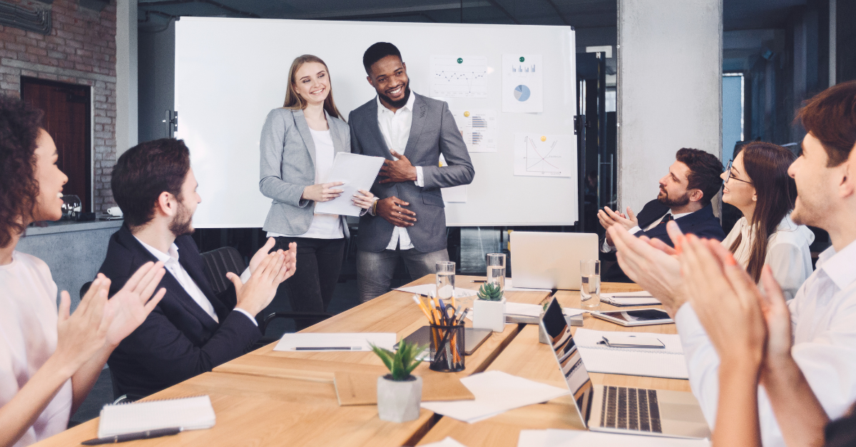 Two people making a presentation to fellow employees sitting at a table.
