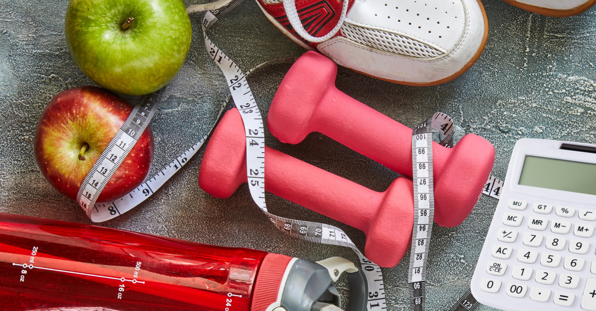 a collection of hand weights, a water bottle, tape measure, apple and calculator.