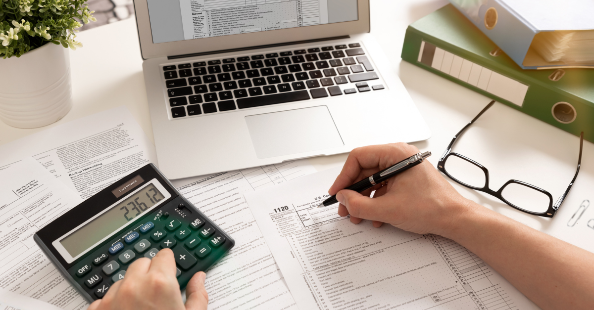 A person working on tax forms, in front of a computer and using a calculator.