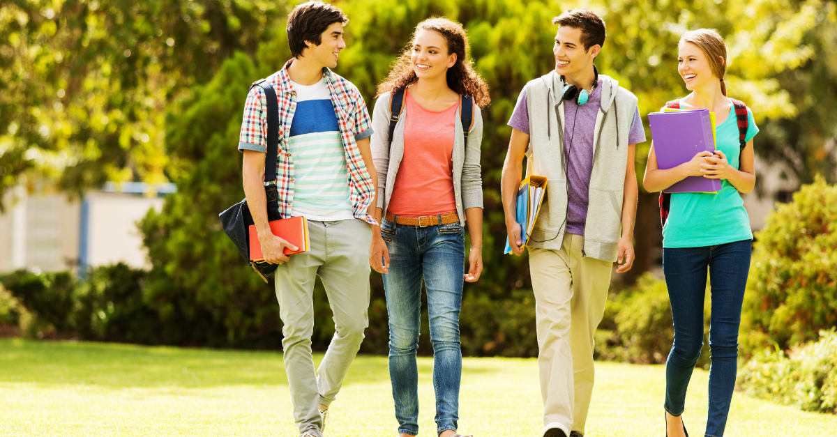 college kids with books and bags walking on a grassy area.