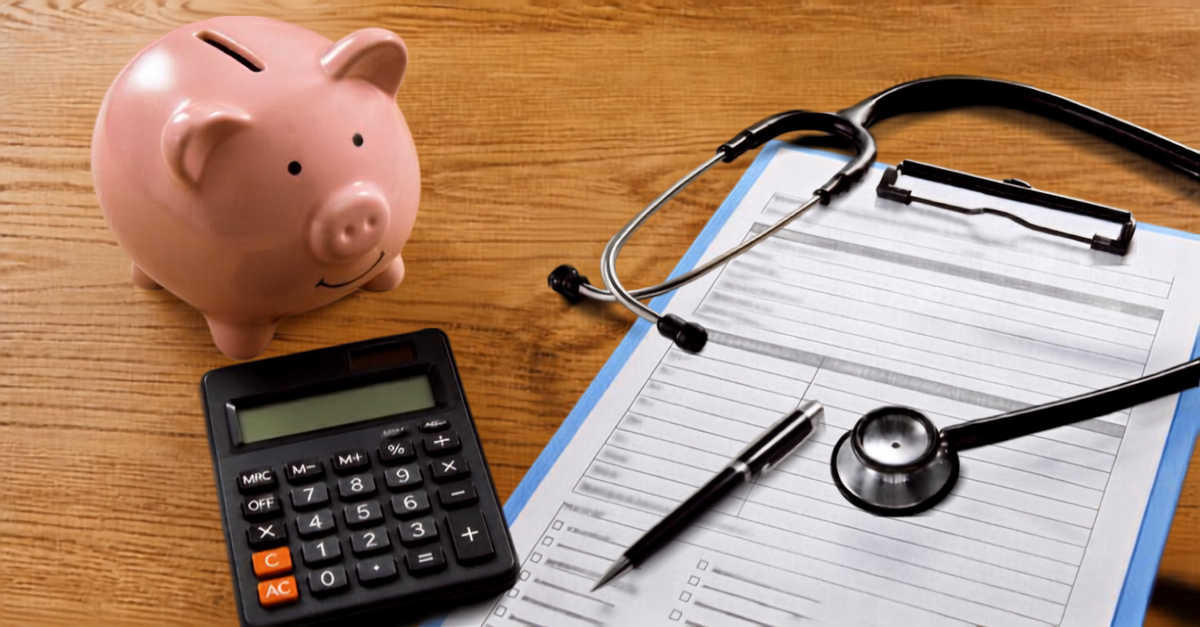 A piggy bank, stethoscope, calculator and pen with clipboard are arranged on a table
